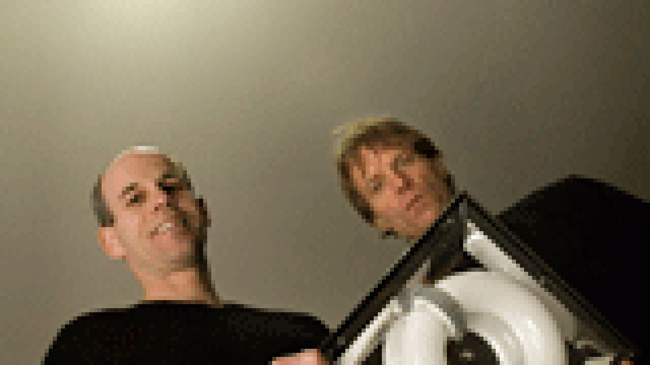 Chris Cioni, left, and Michael Simonovitch display an energy-saving fluorescent light, the kind that is shining above them in the north entry garage. The light is at 100 percent power, because a sensor detects the men standing underneath. But, w