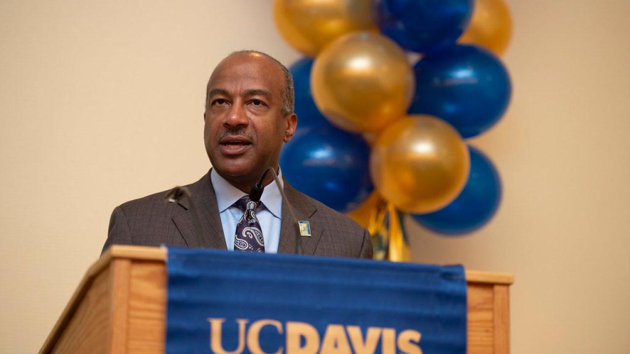 Chancellor Gary S. May at podium with blue and gold balloons in background.