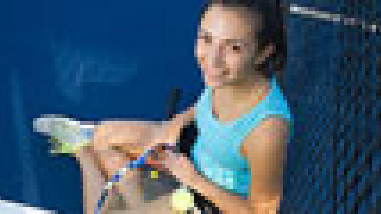 Woman in a tennis outfit with a racket and ball sitting