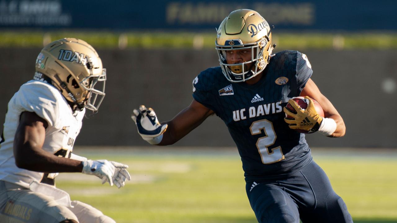 A UC Davis football player carries the ball past a defender