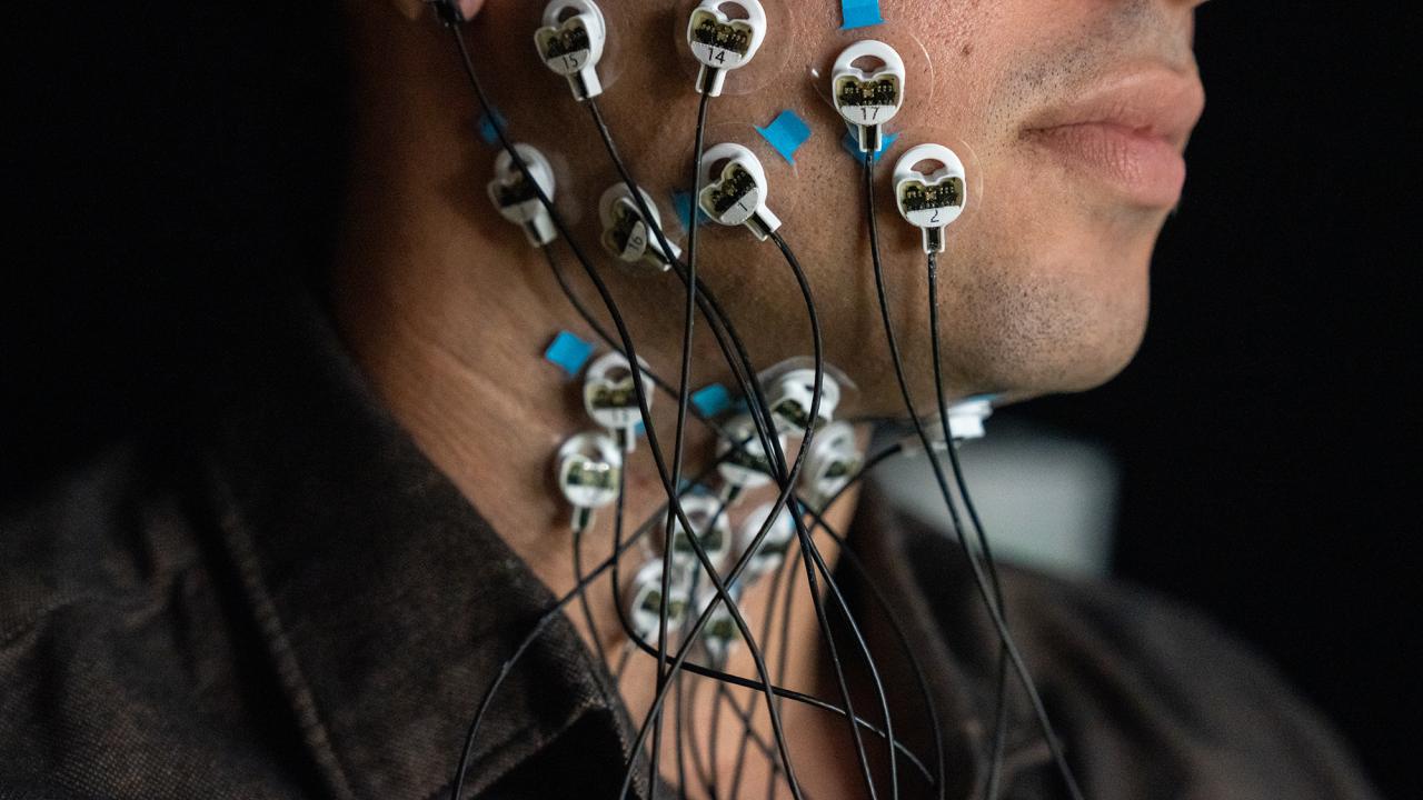 Side view of a young man's face from upper chest to chin. Attached to the skin are several small round disks with wires attached. 