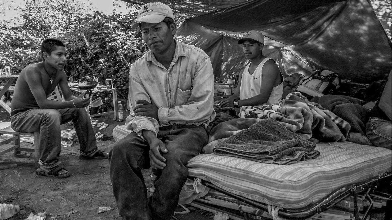 migrant workers under tarps in tent in black and white photo