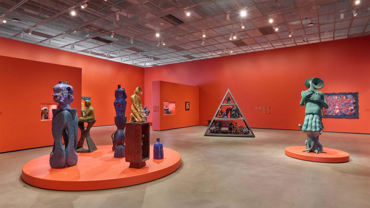 Contemporary gallery with bright orange walls, large colorful sculptural figures on round plinths