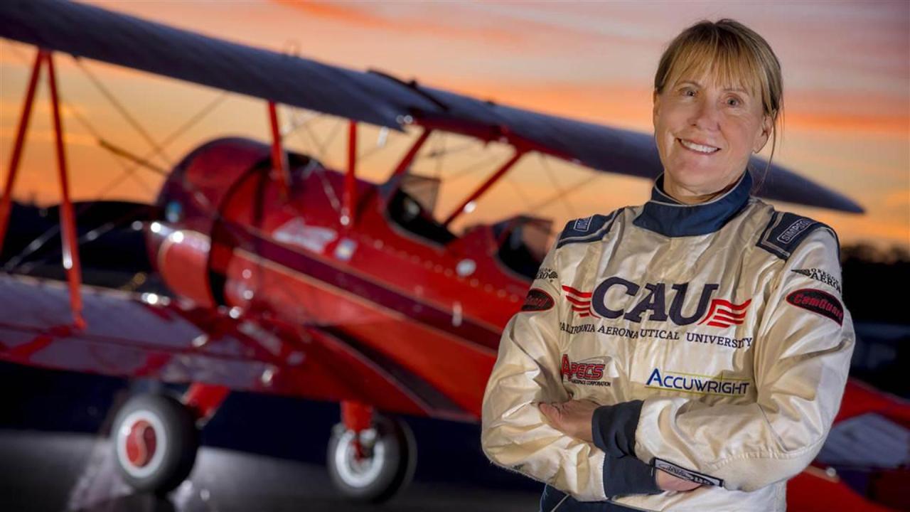 A woman in a flight suit stands in front of a red biplane.