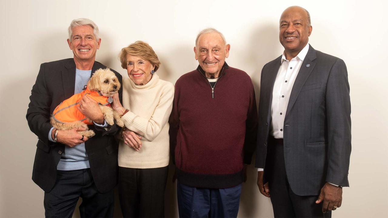 Four people pose for a photo while one holds a small dog