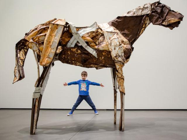 young boy under horse sculpture
