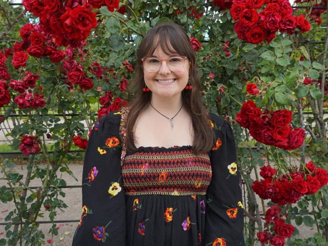 Woman stands in front of a wall of flowers