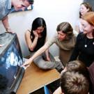 Photo: Woman  pointing to a television screen as younger woman watches