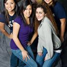 Photo: Four female students grouped below a male student holding a video camera. They are all smiling for the camera.