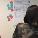 Three women look at wall display with small notes around it.