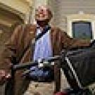 Clarence Walker standing holding his bike in front of a Victorian home