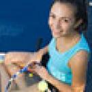 Woman in a tennis outfit with a racket and ball sitting