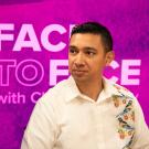 In front of a purple backdrop bearing the Face to Face wordmark logo sits a man in a buttoned white shirt with a design with birds vertically running along its right side. 