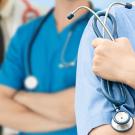 Health professions students from disadvantaged backgrounds often faced childhood adversity, a UC Davis study suggests. Three health professionals in white lab coats and blue scrubs stand next to each other. One holds a stethoscope.