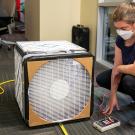 A woman kneels next to a box with air filters on it to monitor the air quality of a room