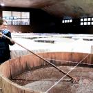 A person stirs something liquid in a big vat inside an industrial room.