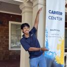 Nick Conti stretches upward to show off a tall banner with the Career Center name.