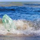 Green plastic jug tossed in foamy surf as waves crash on a beach