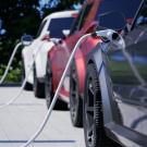 Three electric vehicles charging at a station on a sunny day, surrounded by greenery.