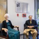 Elderly man and woman seated in a modern office space, smiling and dressed formally.