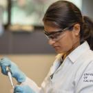 Researcher in a UC‑branded lab coat and safety gear pipetting liquid into a small container at a laboratory
