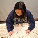 Student with long dark hair and sweatshirt works on plans