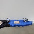 An abstract art installation featuring blue, black, and white forms arranged on the floor. with tile, duck decoys and other forms.