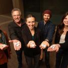 Portrait of five people standing in a group, each holding out a hand with white cubes toward the camera.