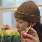 Young person in brown beanie focused while tending pink flowers in greenhouse — photo