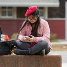 A student wearing a beret uses their smartphone outside of the UC Davis Craft Center.