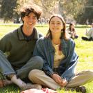 Two students sit cross-legged on the Quad in the sun