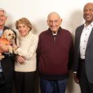 Four people pose for a photo while one holds a small dog