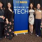 Six people pose for photo in front of banner