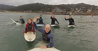 Several surfers in wet suits in the ocean with a surf board in the foreground